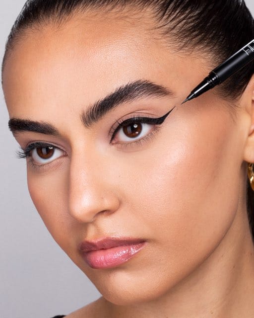 A model applying a black liquid eyeliner wing with the pen still in frame.
