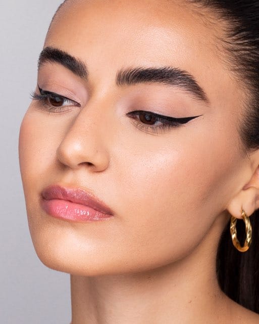 A three-quarter beauty portrait of a finished black winged liner, with a gold hoop earring.