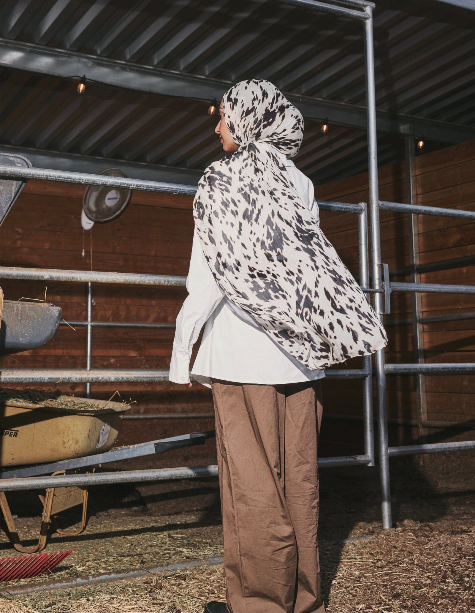 Campaign photograph: a model seen from behind in a speckled-hide scarf, standing in a stable.